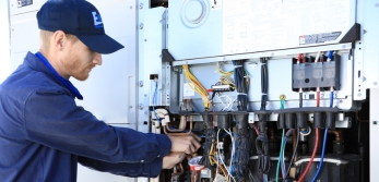 Male service technician touching wires on an HVAC unit.